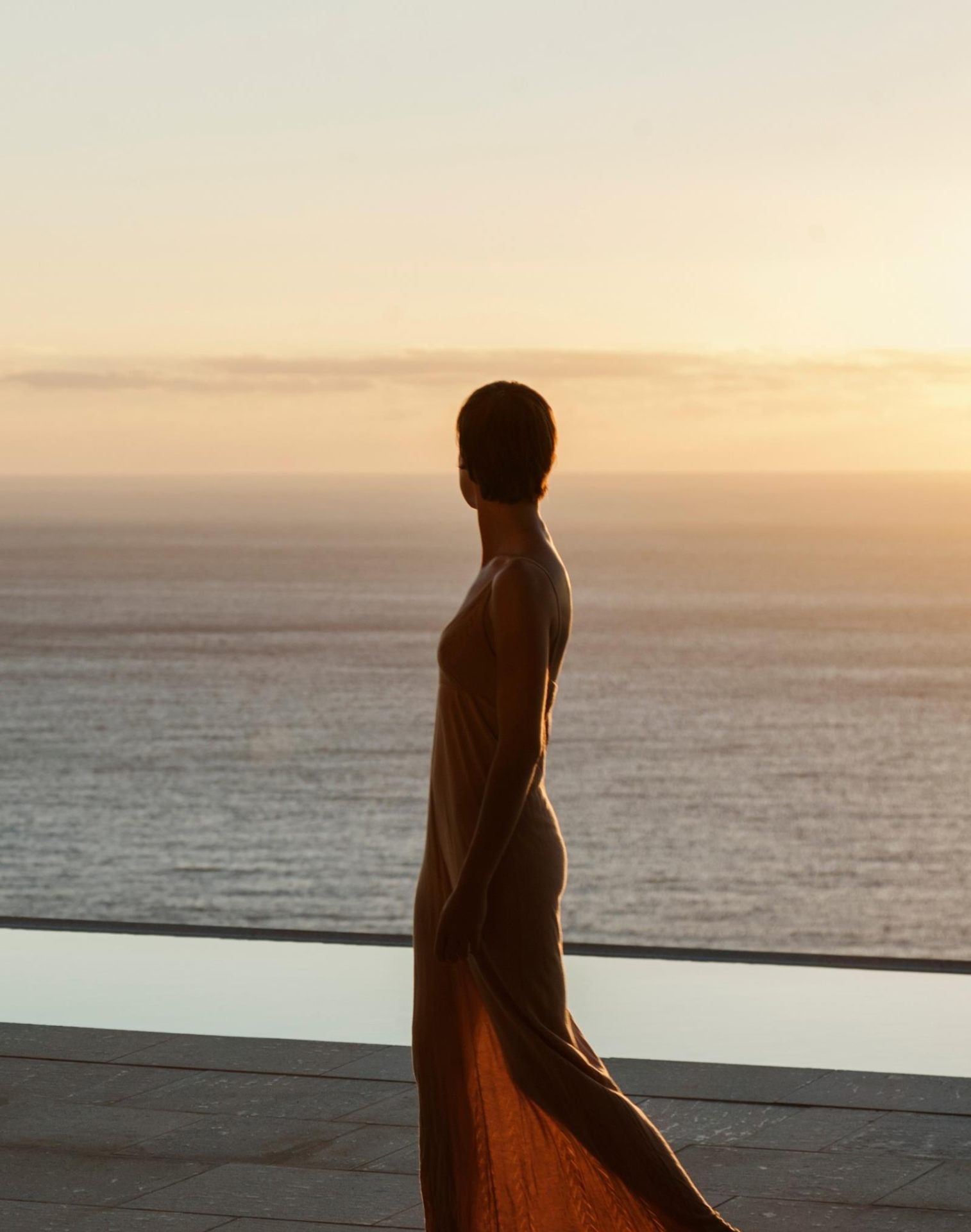 Mulher contemplando o pôr do sol sobre o mar da Enseada Azul